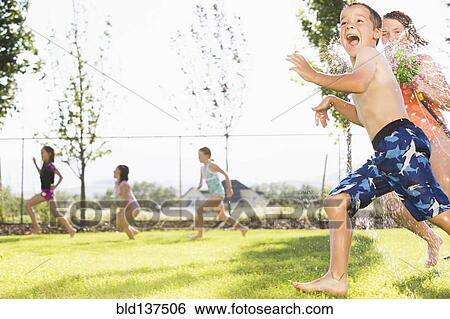 Stock Photograph - Caucasian children playing in sprinkler in backyard. Fotosearch