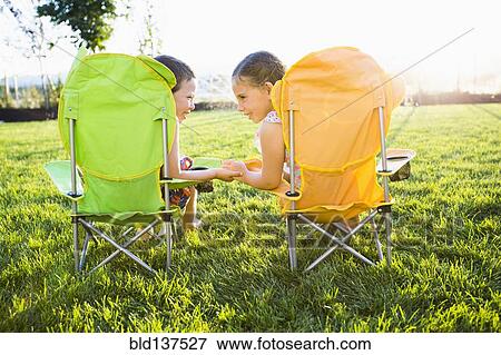 Stock Photo - Caucasian children relaxing in lawn chairs in backyard. Fotosearch