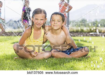 Stock Photography - Caucasian children sitting in sprinkler in backyard. Fotosearch