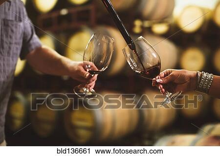 Stock Image - Caucasian couple tasting wine in cellar. Fotosearch