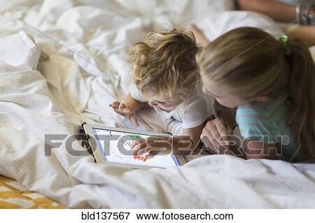 Caucasian girl and toddler brother using tablet computer on bed View Large Photo Image Stock Photo - Caucasian girl and toddler brother using tablet computer on bed. Fotosearch