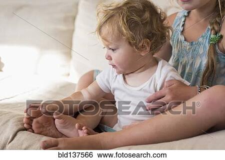 Stock Photograph - Caucasian girl and toddler brother sitting on bed. Fotosearch