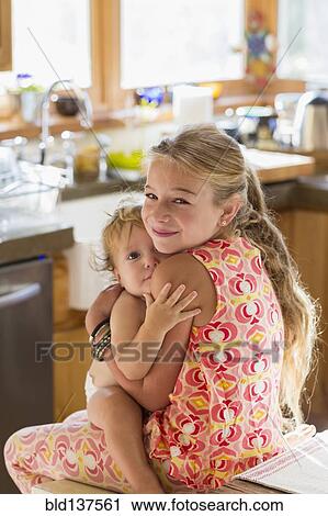 Stock Image - Caucasian girl holding toddler brother in kitchen. Fotosearch