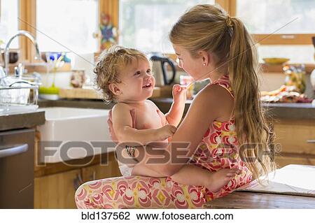 Stock Image - Caucasian girl holding toddler brother in kitchen. Fotosearch
