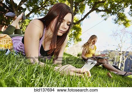 Picture - Caucasian girl using cell phone in grass. Fotosearch