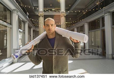 Stock Image - Caucasian man carrying blueprints in building. Fotosearch