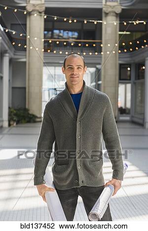 Stock Image - Caucasian man carrying blueprints in building. Fotosearch
