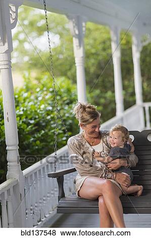 Stock Photo - Caucasian mother and toddler sitting in swing on porch. Fotosearch