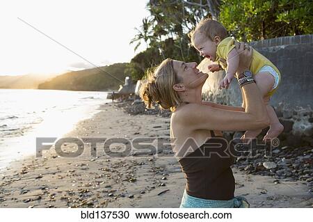 Stock Image - Caucasian mother holding baby on beach. Fotosearch