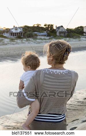 Stock Image - Caucasian mother holding baby on beach. Fotosearch