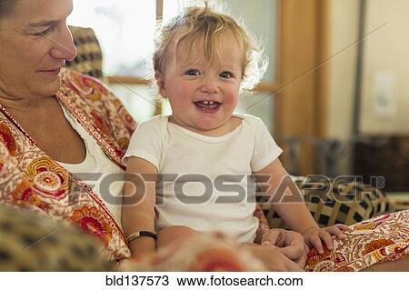 Stock Image - Caucasian mother holding toddler in living room. Fotosearch