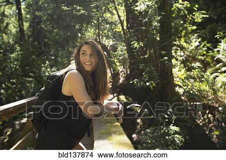 Picture - Caucasian woman standing on wooden bridge in forest. Fotosearch