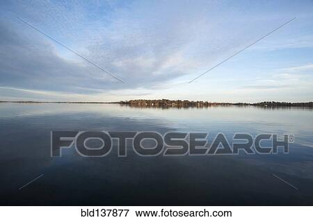 Stock Photo - Clouds and sky reflected in still lake in rural landscape. Fotosearch