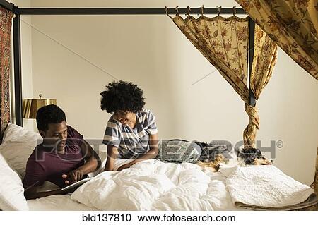 Stock Image - Couple and dog relaxing on bed. Fotosearch