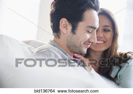 Picture - Couple smiling together on sofa. Fotosearch