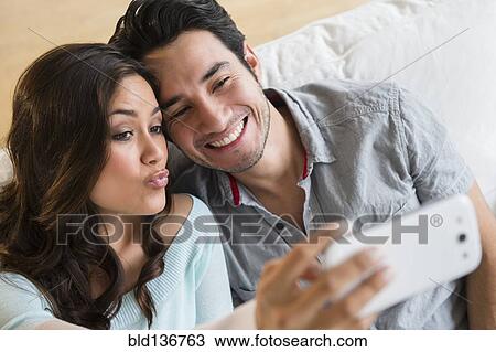 Stock Image - Couple taking pictures together on sofa. Fotosearch