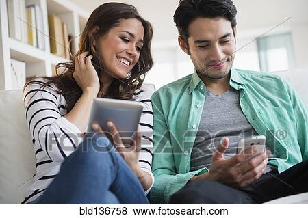 Stock Photo - Couple using technology together on sofa. Fotosearch