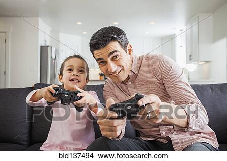 Picture - Father and daughter playing video games in living room. Fotosearch