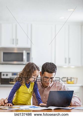 Stock Photograph - Father and daughter using laptop in kitchen. Fotosearch