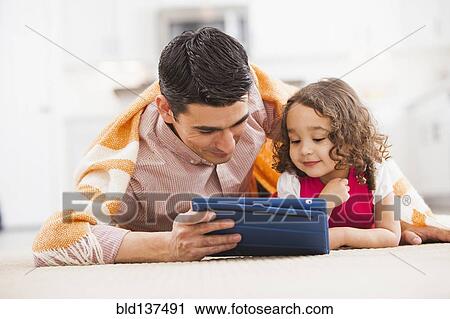 Stock Image - Father and daughter using tablet computer on living room floor. Fotosearch
