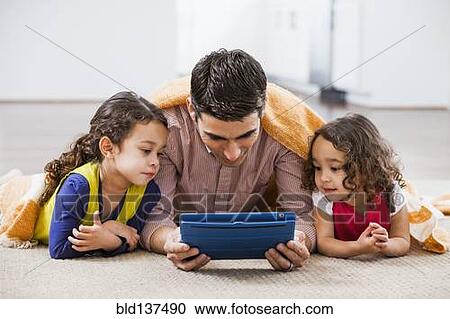 Stock Image - Father and daughters using tablet computer on living room floor. Fotosearch