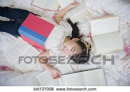Stock Photo - Filipino girl laying in bed with books. Fotosearch