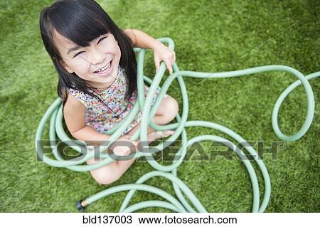 Stock Image - Filipino girl playing with hose in backyard. Fotosearch