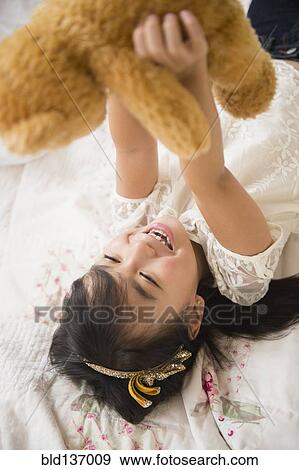 Filipino girl playing with teddy bear on bed View Large Photo Image Stock Photo - Filipino girl playing with teddy bear on bed. Fotosearch