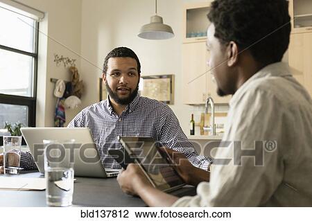 Stock Image - Friends using technology at breakfast table. Fotosearch