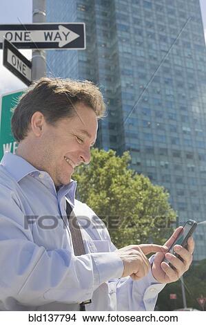 Hispanic businessman using cell phone on city street View Large Photo Image Picture - Hispanic businessman using cell phone on city street. Fotosearch