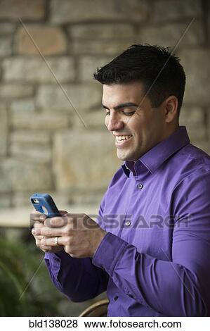 Stock Photo - Hispanic businessman using cell phone indoors. Fotosearch