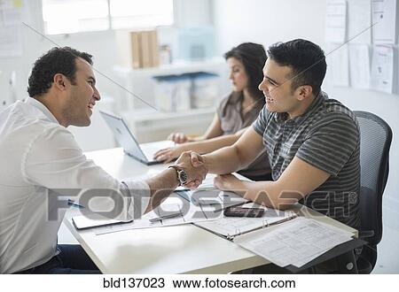 Stock Image - Hispanic businessmen shaking hands in office. Fotosearch