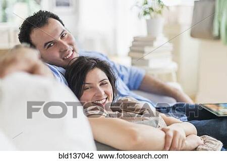 Stock Image - Hispanic couple relaxing together on sofa. Fotosearch