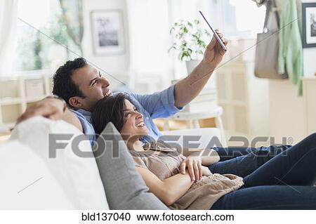 Stock Image - Hispanic couple using tablet computer on sofa. Fotosearch