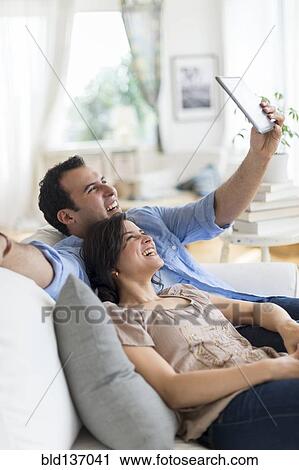 Stock Image - Hispanic couple using tablet computer on sofa. Fotosearch
