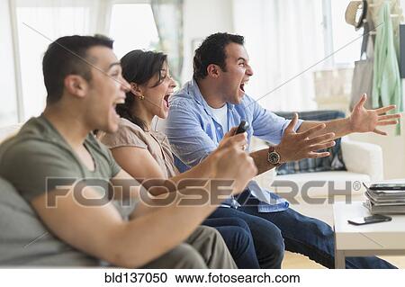 Hispanic friends cheering at television in living room View Large Photo Image Stock Image - Hispanic friends cheering at television in living room. Fotosearch
