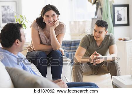 Stock Image - Hispanic friends talking in living room. Fotosearch