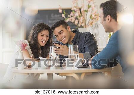 Stock Photograph - Hispanic friends using cell phone in cafe. Fotosearch