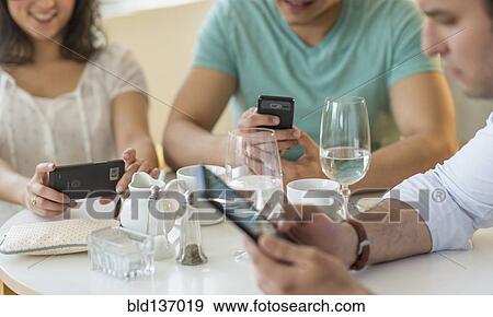 Hispanic friends using cell phones in cafe View Large Photo Image Stock Photo - Hispanic friends using cell phones in cafe. Fotosearch