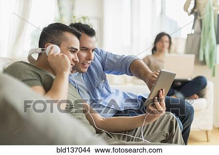 Picture - Hispanic friends using tablet computer on sofa. Fotosearch