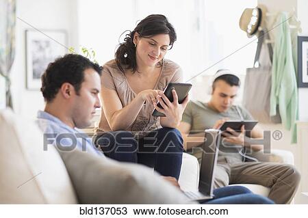 Stock Image - Hispanic friends using technology in living room. Fotosearch