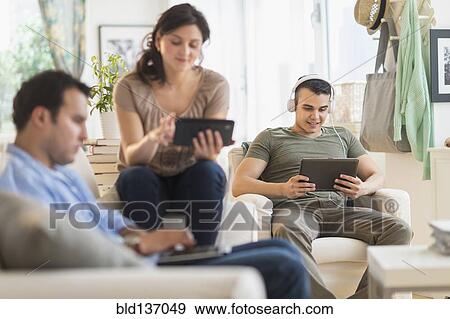 Stock Photo - Hispanic friends using technology in living room. Fotosearch