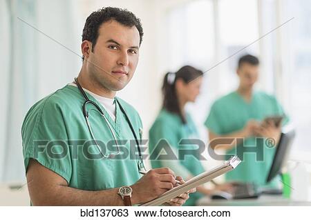 Stock Image - Hispanic nurse reading medical chart in hospital. Fotosearch