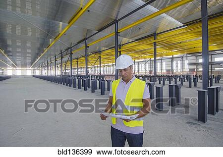 Stock Photo - Hispanic worker reading blueprints in warehouse. Fotosearch