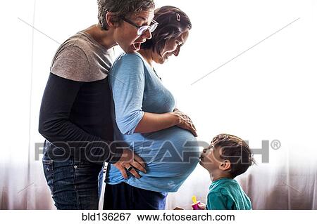 Stock Photo - Lesbian couple with son standing by window. Fotosearch