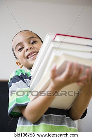 Stock Image - Mixed race boy carrying stack of books in class. Fotosearch