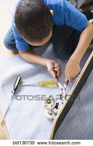 Stock Photo - Mixed race boy fixing skateboard. Fotosearch