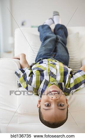 Stock Photography - Mixed race boy laying upside-down on armchair. Fotosearch