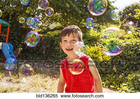 Stock Photography - Mixed race boy playing with bubbles in backyard. Fotosearch