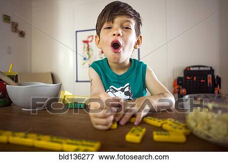 Stock Photo - Mixed race boy playing with dominoes at kitchen table. Fotosearch